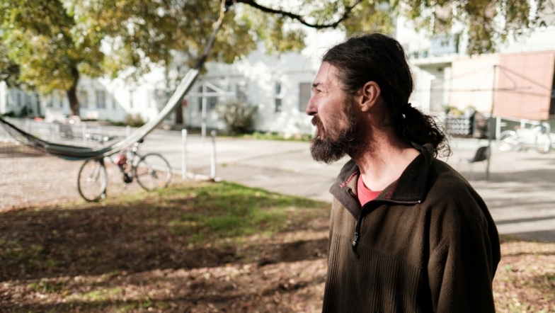 Middle aged white man stands in front of a hammock and bicycle