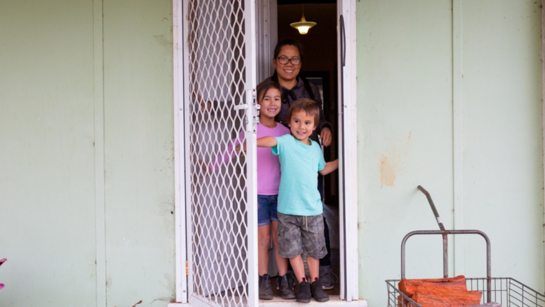 Woman of colour standing in her doorway with two children