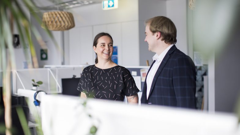 Justice Connect lawyers Samantha Sowerwine and Cameron Laverty stand in the Justice Connect office talking to one another.