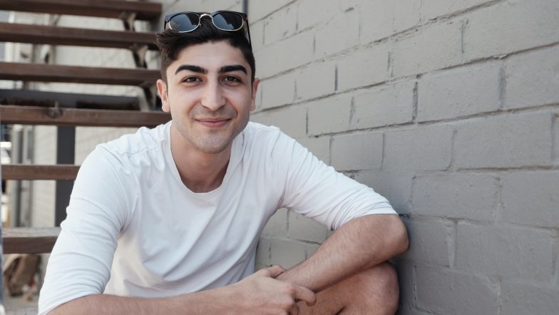 Young man wearing a white tshirt smiles while sitting on a set of stairs